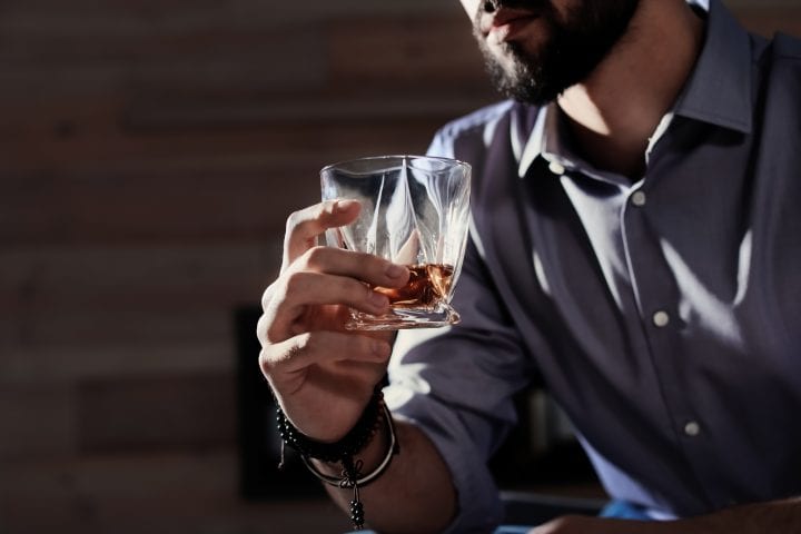 Man with glass of whiskey at home, closeup. Space for text