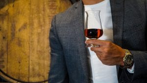 Man holding a glass of whiskey standing against a cask.